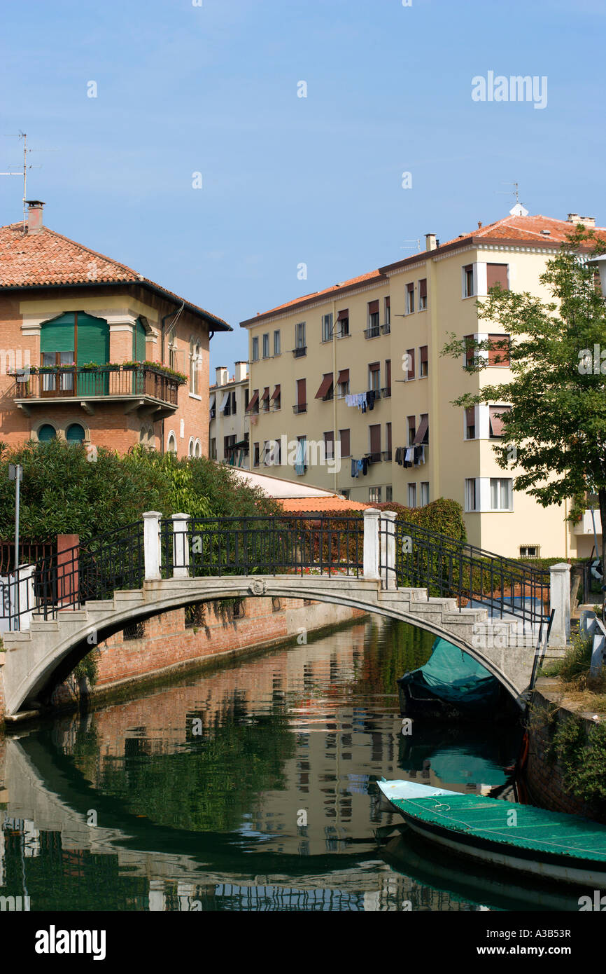 Italien Venetien Venedig Lido Canal Wasserstraße zwischen Häusern mit Fußgängerbrücke über Wasser neben festgemachten Boote Stockfoto