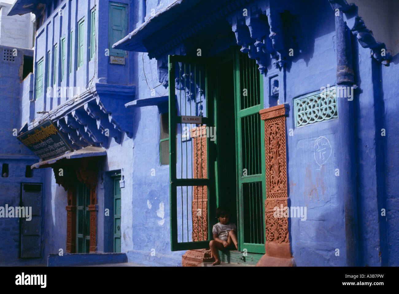 Indien in Südasien Rajasthan Jodhpur Religion hinduistischen Brahmanen blaues Haus mit Kind sitzt in Tür mit grünen Rahmen Stockfoto