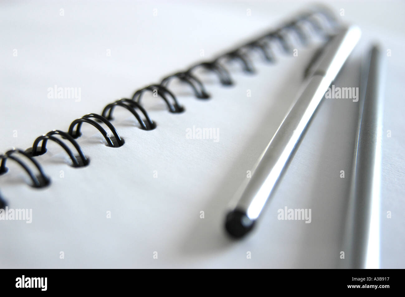 Weißes Notizbuch mit schwarzer Spiralbindung, Edelstahlstift und Silberstift. Aufnahme mit geringer Schärfentiefe. Stockfoto