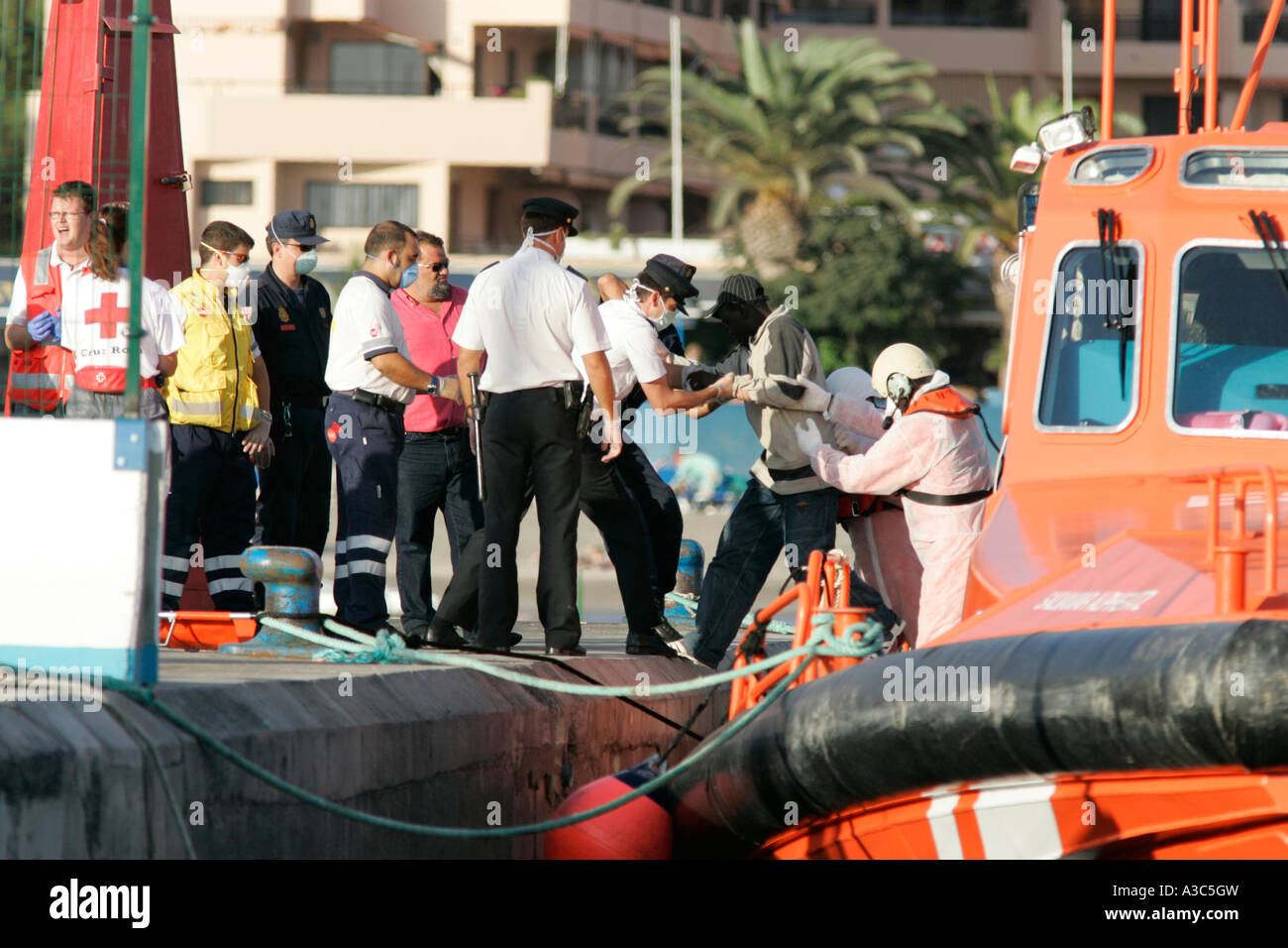 die spanische Polizei und Beamte in Schutzkleidung und Masken auf orange Maritimo Salvamento Boot begleiten illegale Einwanderer Stockfoto