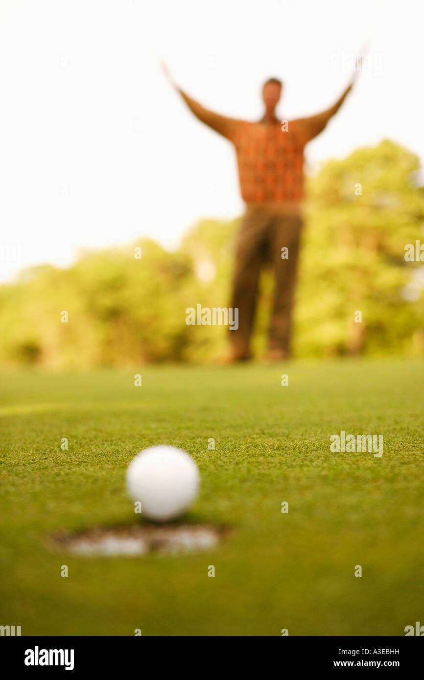 Nahaufnahme eines Golfballs am Rand eines Lochs mit einem Mann, der seine Arme im Hintergrund Stockfoto