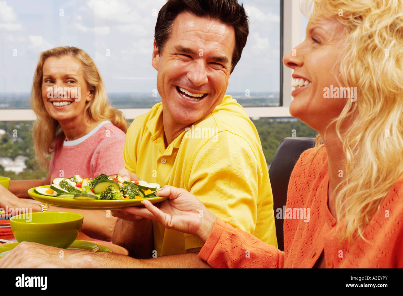 Mitte Erwachsene Frau hält einen Teller Salat und ein älteres Paar am Tisch sitzen Stockfoto