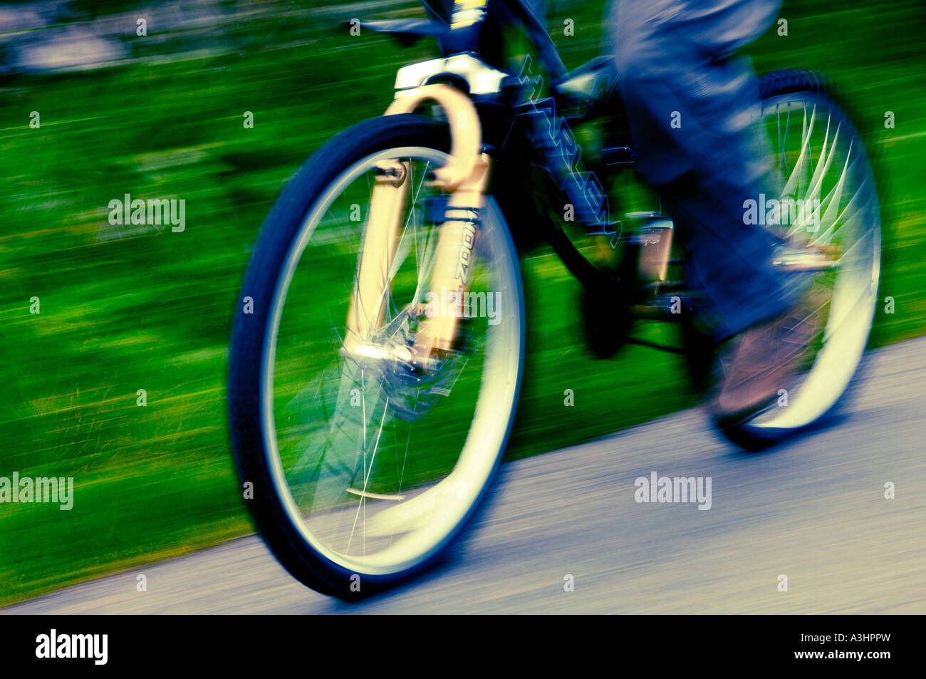 Verschwommenes Filmfoto von den Beinen eines Mannes, der auf einer Landstraße Fahrrad fährt Stockfoto