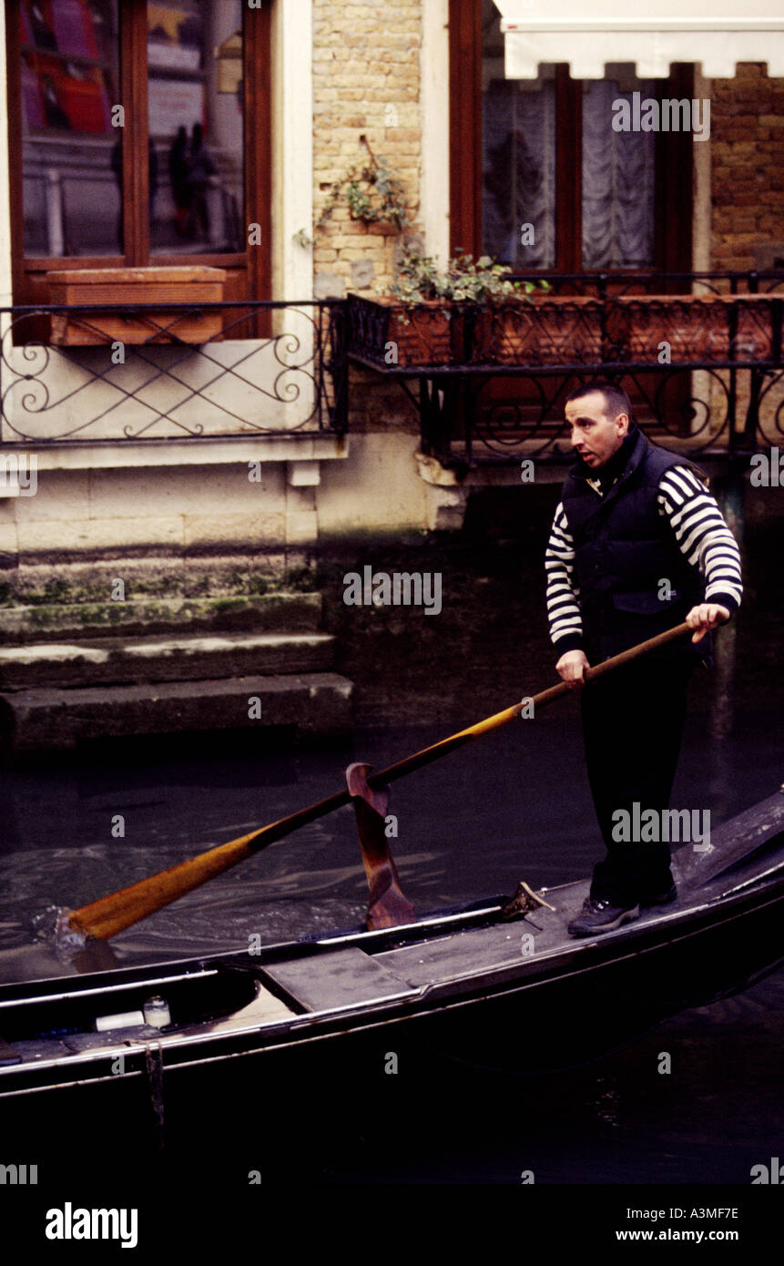 Ein Gondoliere steht auf der Rückseite der seine Gondel auf eines der kleinen Kanäle von Venedig mit typischen Kanal Gebäude im Hintergrund Stockfoto