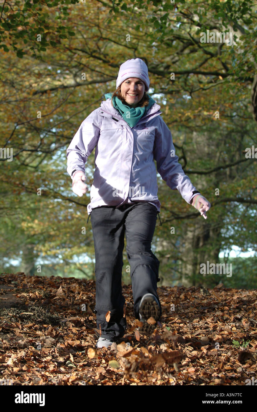Frau, eingehüllt in warme Winterkleidung führt durch Blätter auf Waldboden Stockfoto