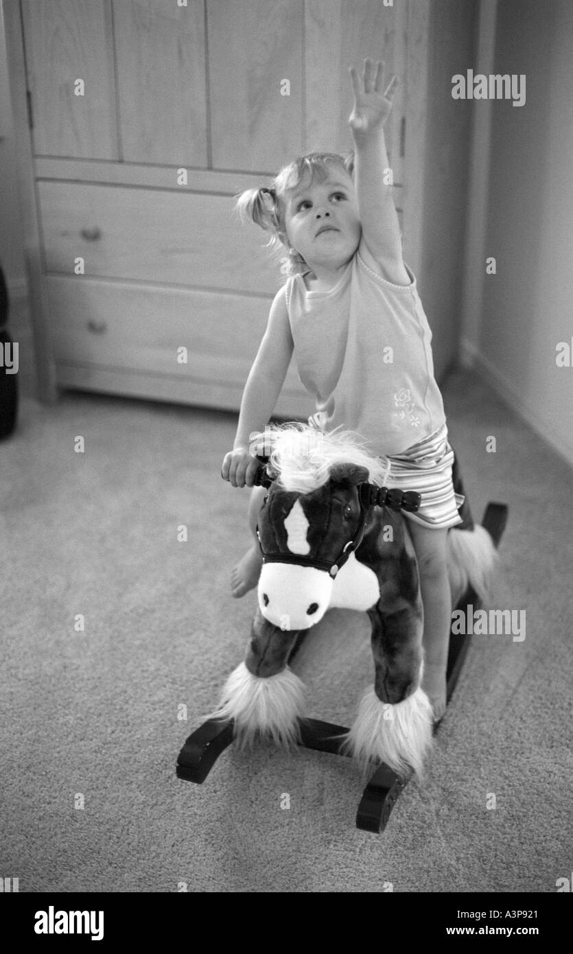 2 Jahre altes Mädchen reiten Schaukelpferd hält einen arm Stockfoto