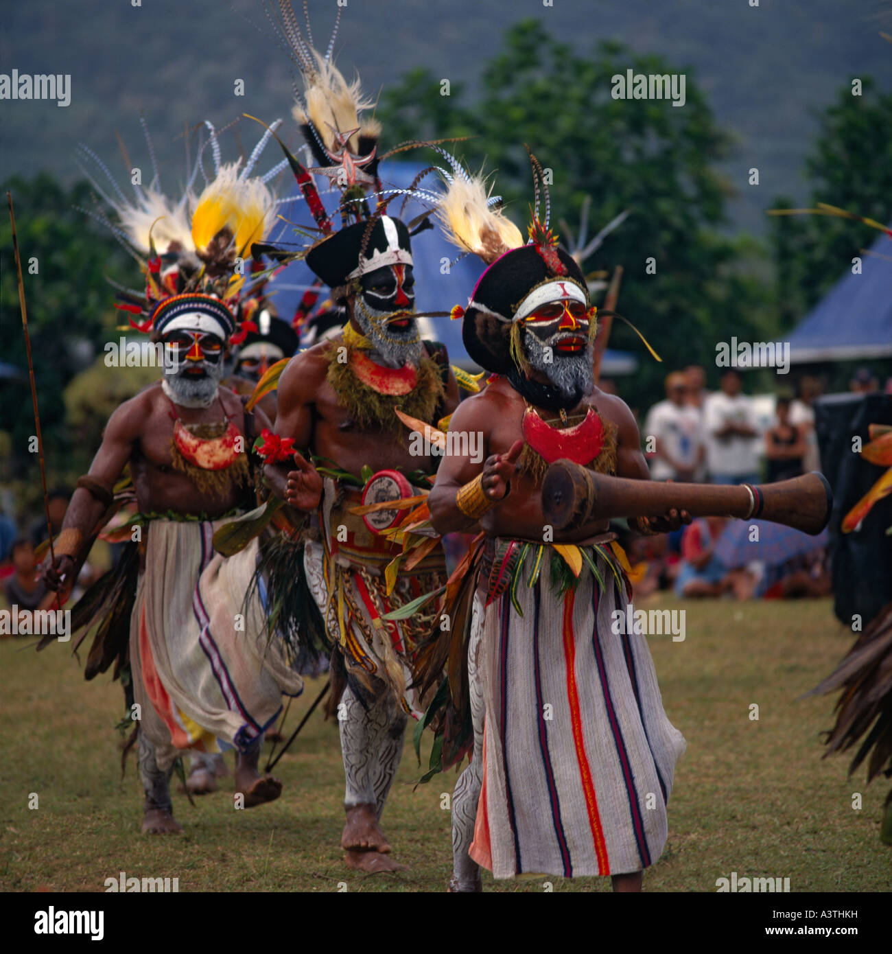 Männliche Engi Stammesangehörigen aus Papua Neuguinea tanzen in schwarz & gefiederten Kopfschmuck und tragen große Medaillons mit aufgemalten Gesichtern Stockfoto