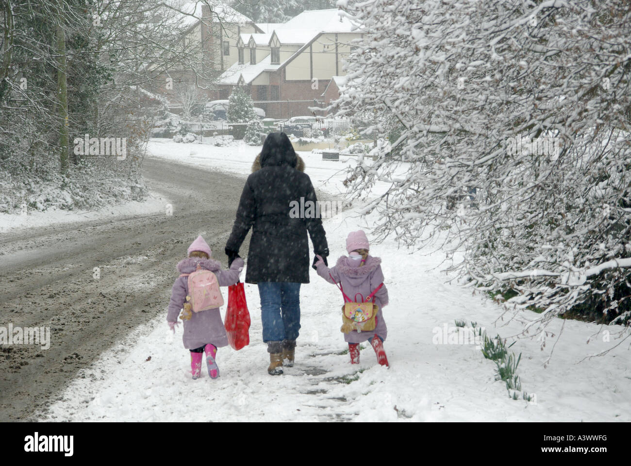 Winter Street Szene kleine Kinder auf dem Bürgersteig im Schnee Hände mit der Mutter auf dem kalten Morgenspaziergang zum Dorf halten Schule Essex England Großbritannien Stockfoto