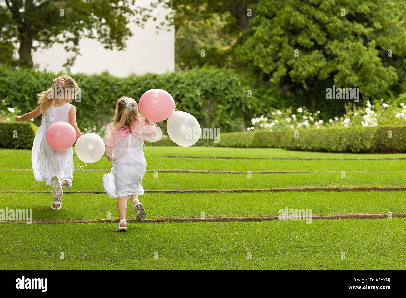 Zwei junge Mädchen im Garten, ausgeführt mit Luftballons, Ansicht von hinten Stockfoto