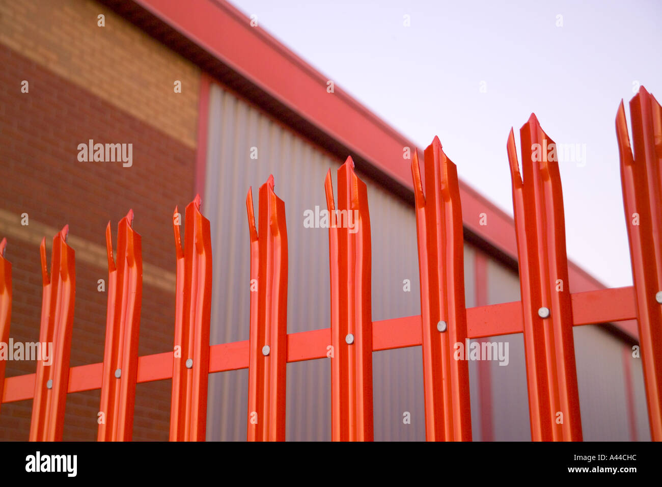 Blick auf roten Sicherheitszaun mit einem roten Ziegel Gebäude dahinter Stockfoto