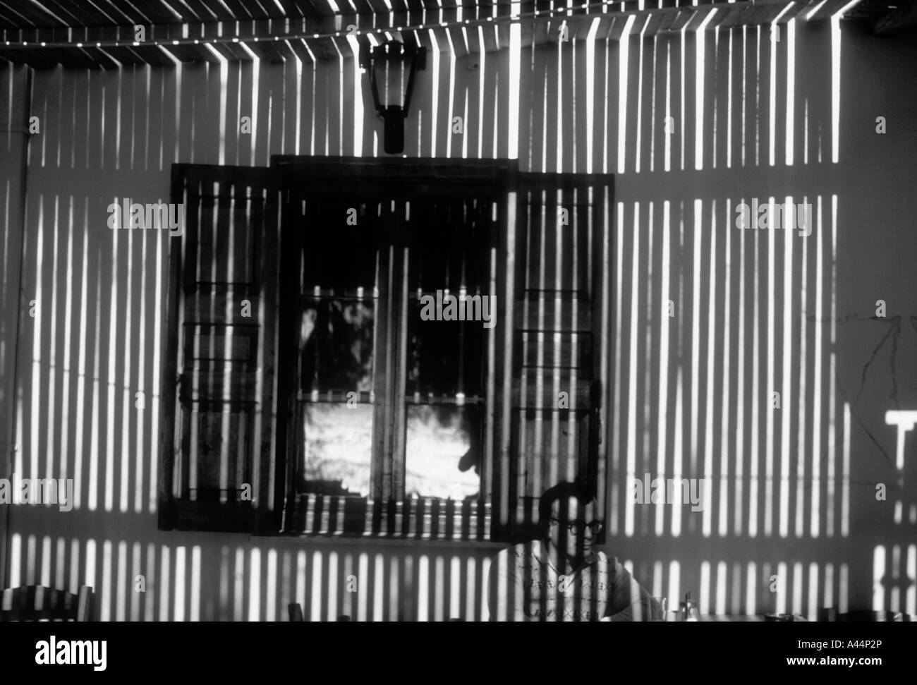 Ein Mann sitzt außen eine Taverne auf der griechischen Insel Santorin, Camoufaged von den Schatten werfen, durch die Überdachung der Terrasse. Stockfoto