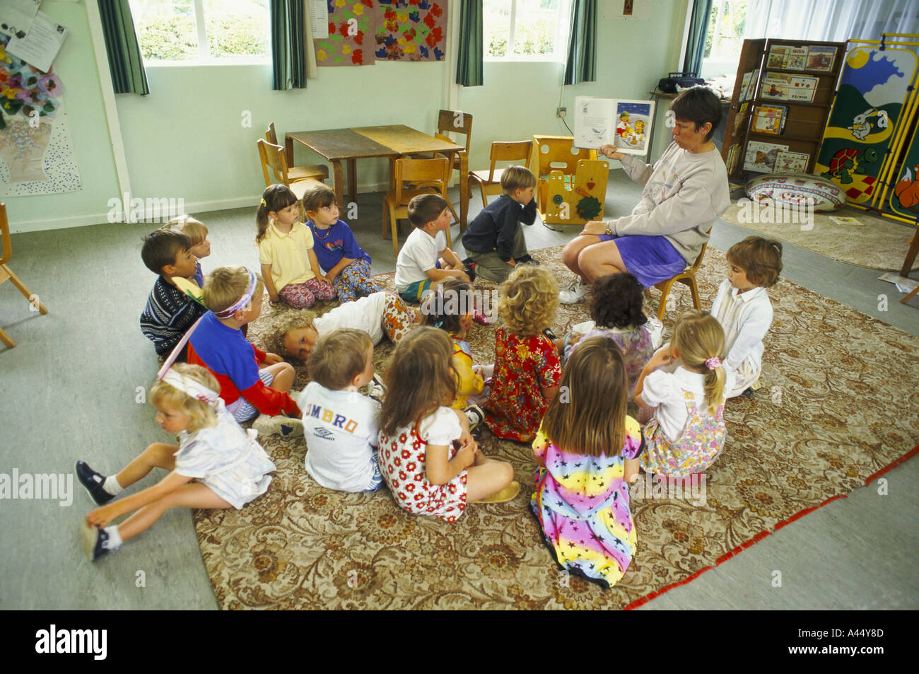 Lehrer liest eine Geschichte vor kleinen Kindern auf dem Boden am Windmühle Spielgruppe Flitwick bedfordshire Stockfoto