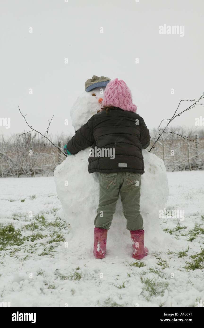 Kindheit-Spaß im Winterschnee mit Kleinkind in grüne Hose umarmt einen Schneemann zu Hause. Stockfoto