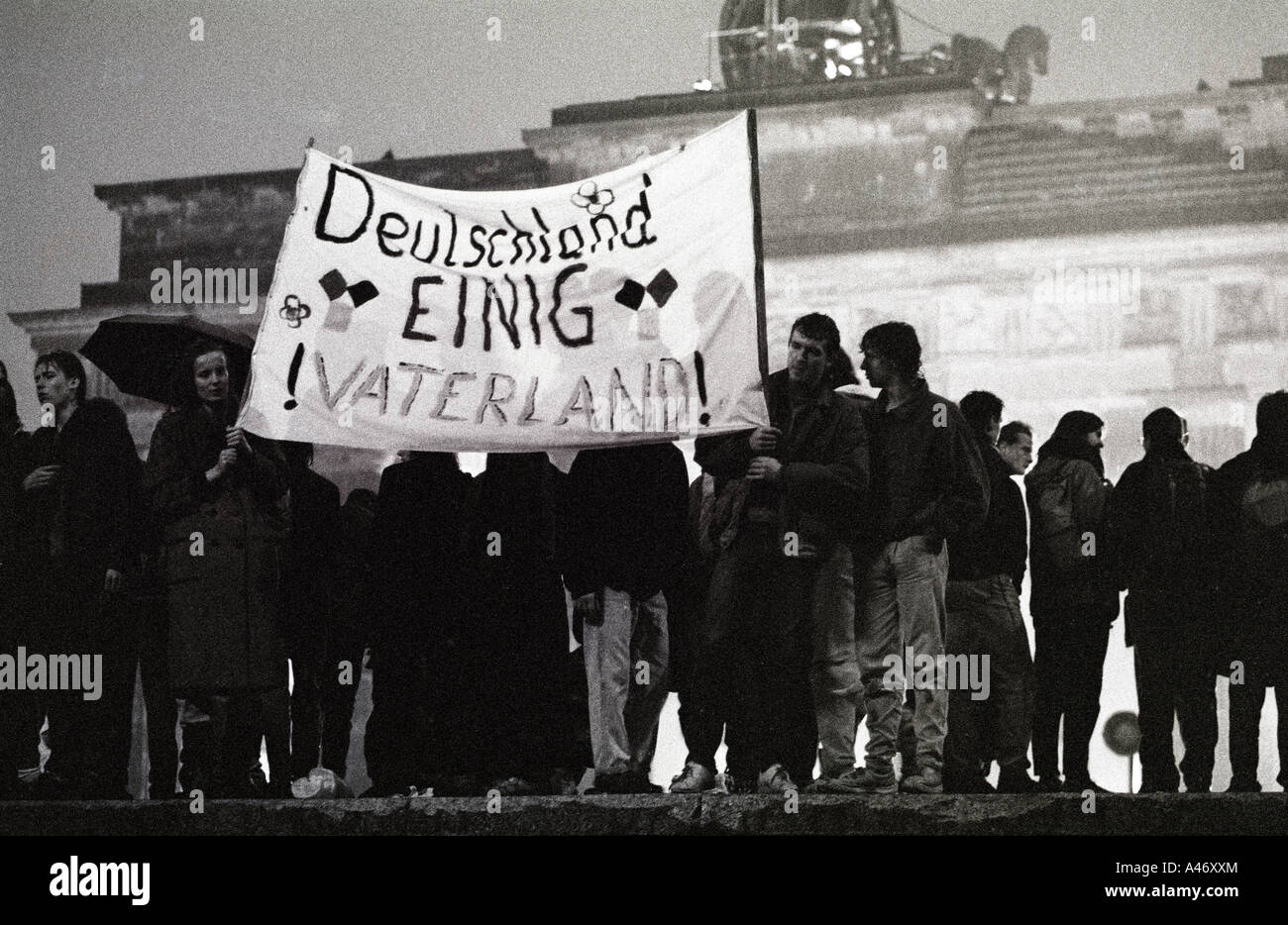 Fall der Berliner Mauer: Menschen aus Ost und West-Berliner auf der Mauer am Brandenburger Tor halten ein transparent Stockfoto