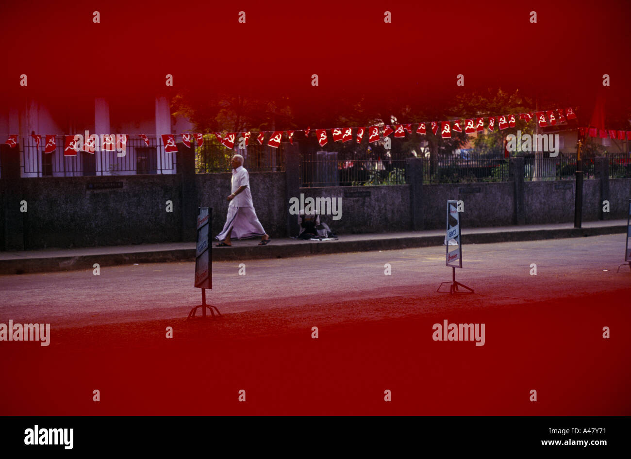 Ein Mann geht vorbei und ignoriert einen Bettler betteln um Almosen unter einer kommunistischen Banner Calicut Indien Stockfoto