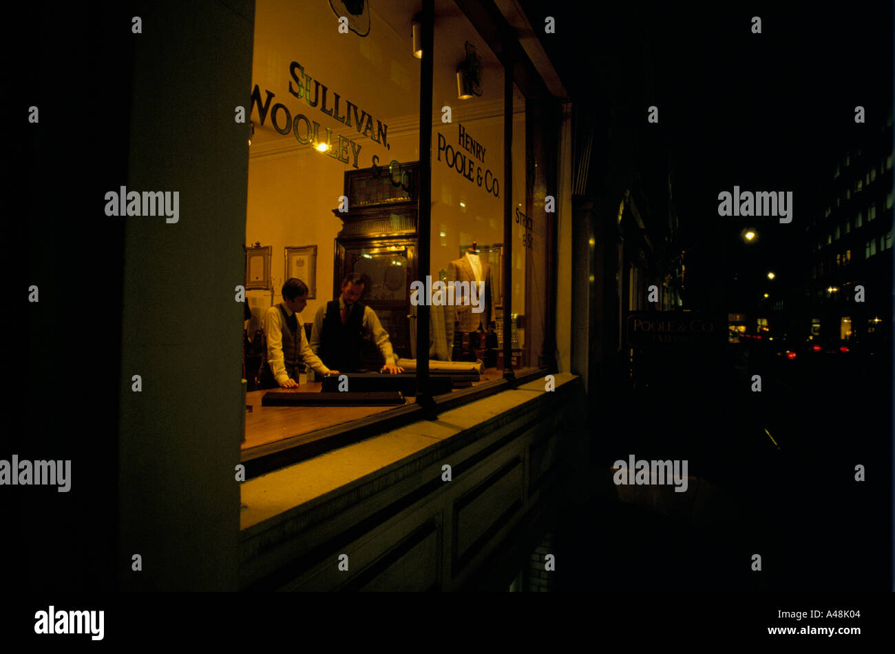 Tailor Shop auf Saville Row London Ladenbesitzer Wahl Kundenstoff hinter Schaufenster in der Nacht Stockfoto