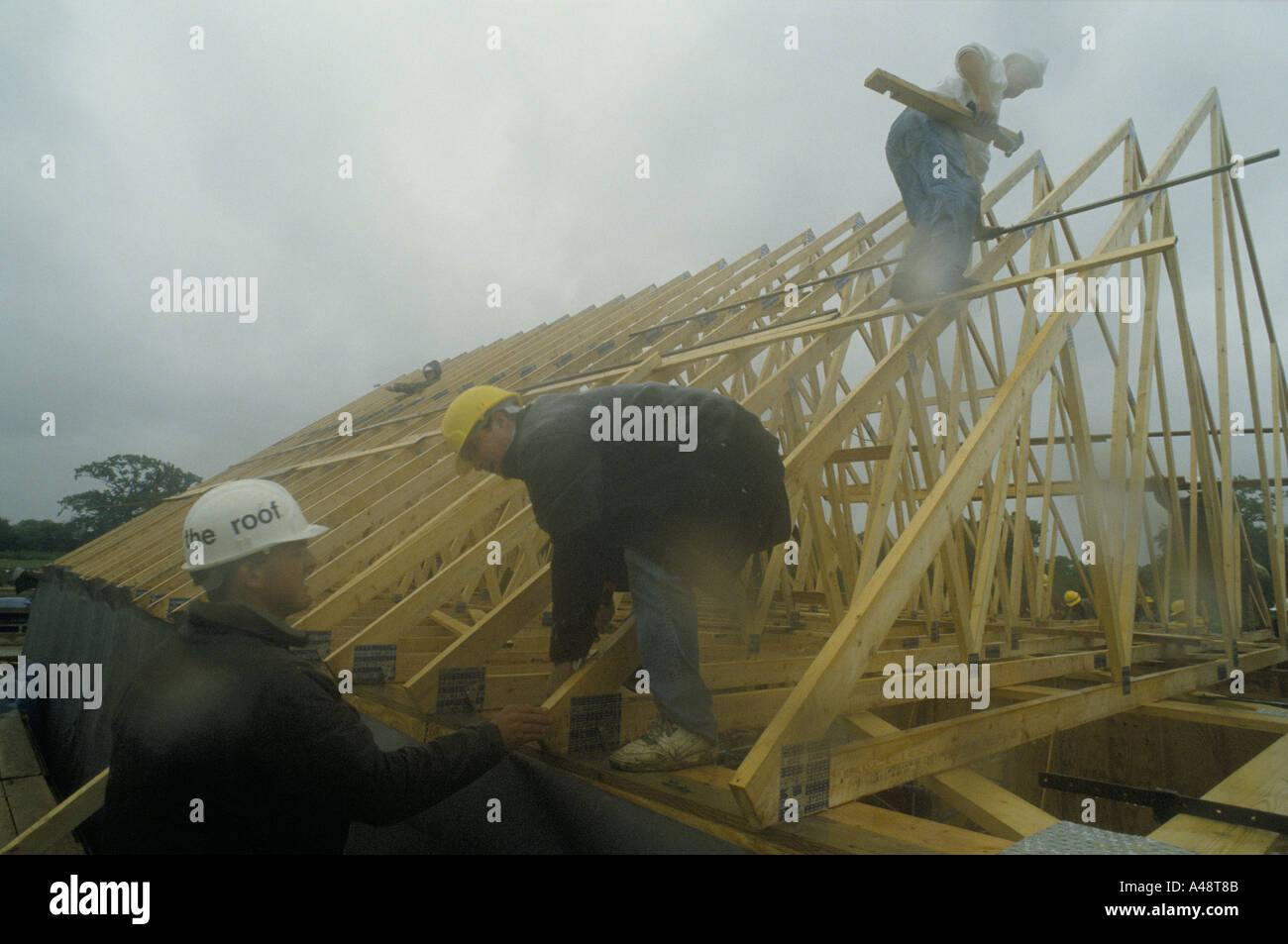 Bauarbeiter mit Schutzhelmen bauen Dachkonstruktionen aus Holz in Regen Stockfoto
