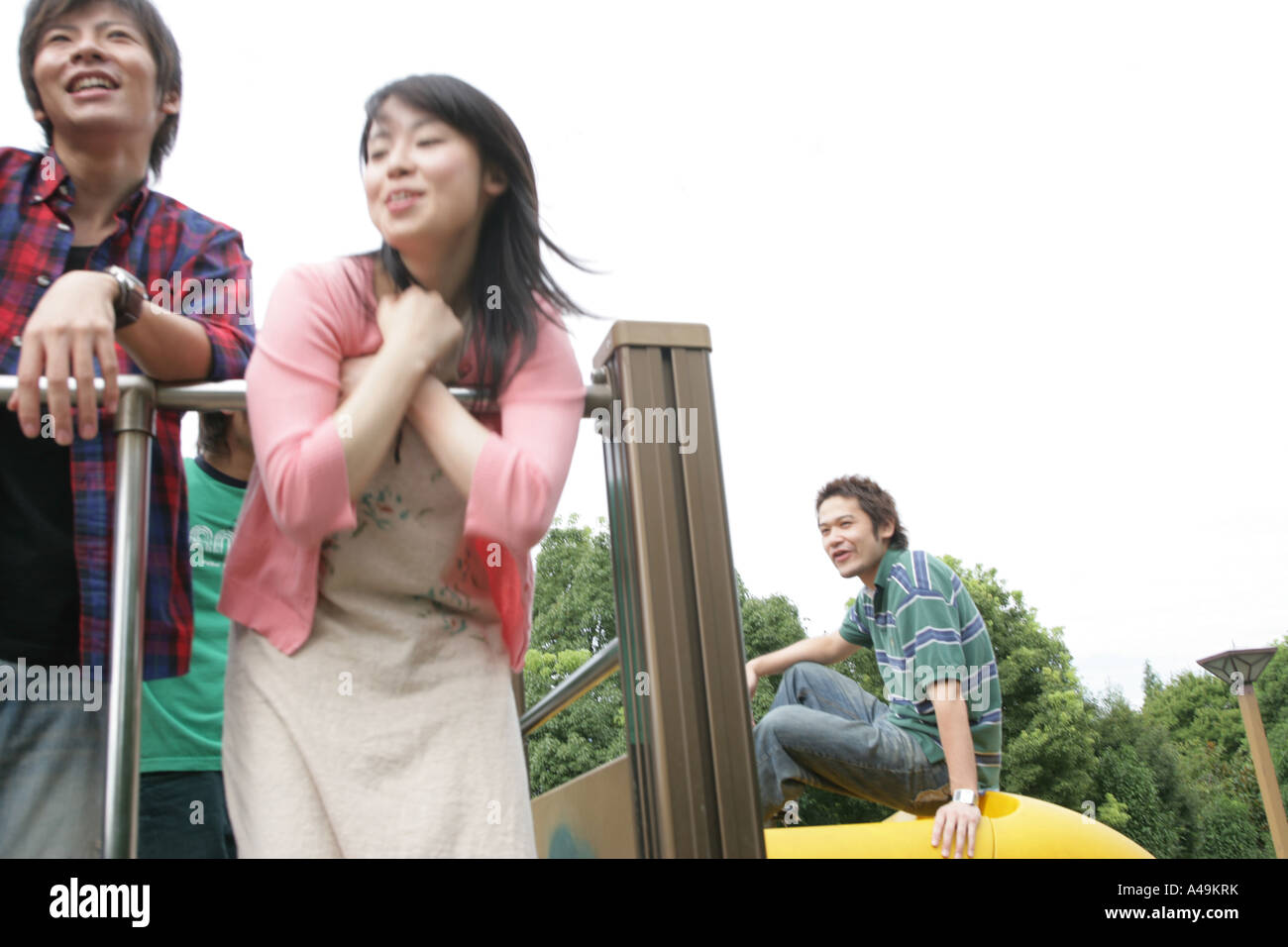 Niedrigen Winkel Ansicht eines jungen Paares, die über ein Geländer mit einem anderen jungen Mann hinter ihnen sitzen nach vorne beugen Stockfoto