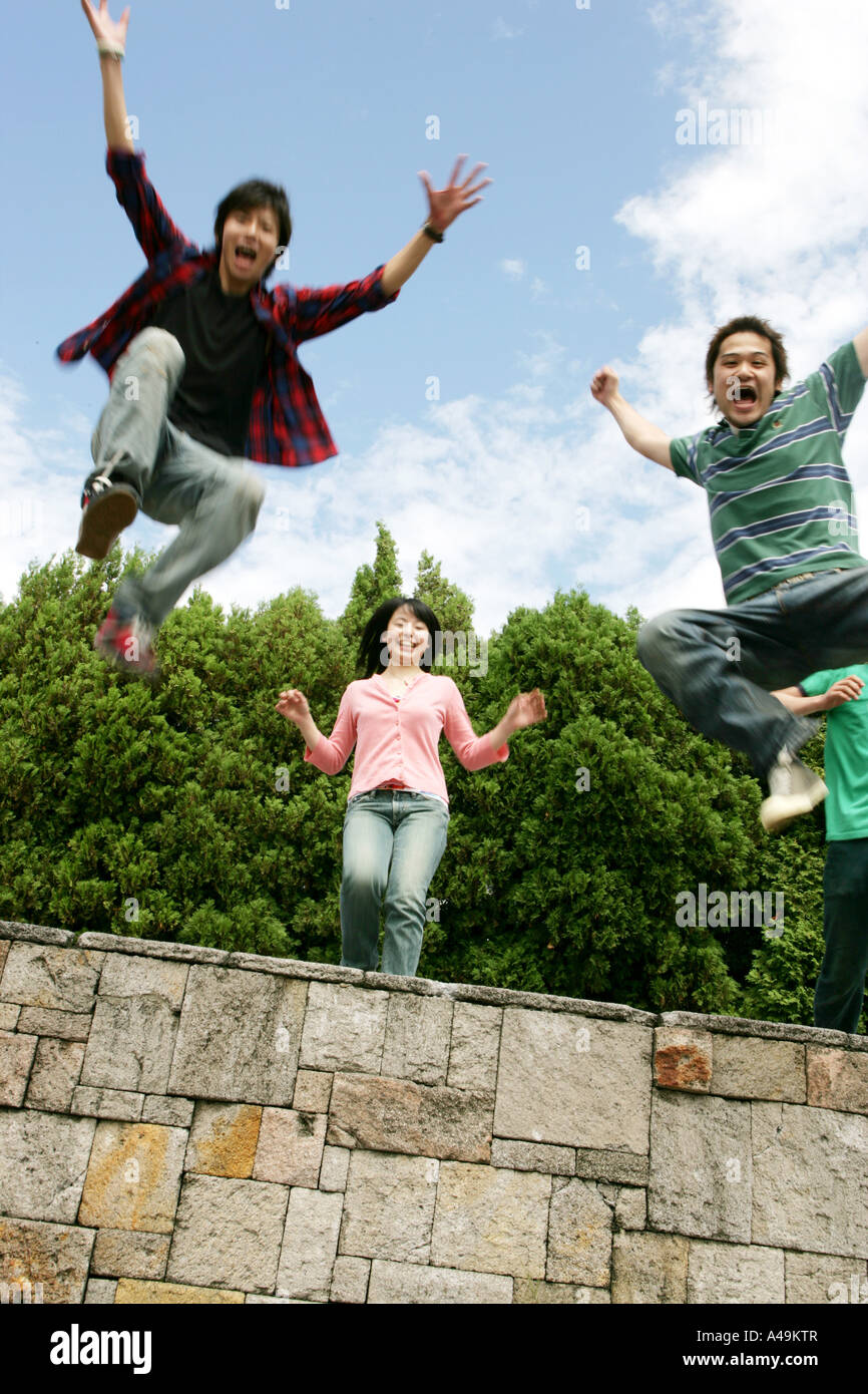 Niedrigen Winkel Blick auf eine junge Frau an einer Wand mit zwei junge Männer springen Stockfoto