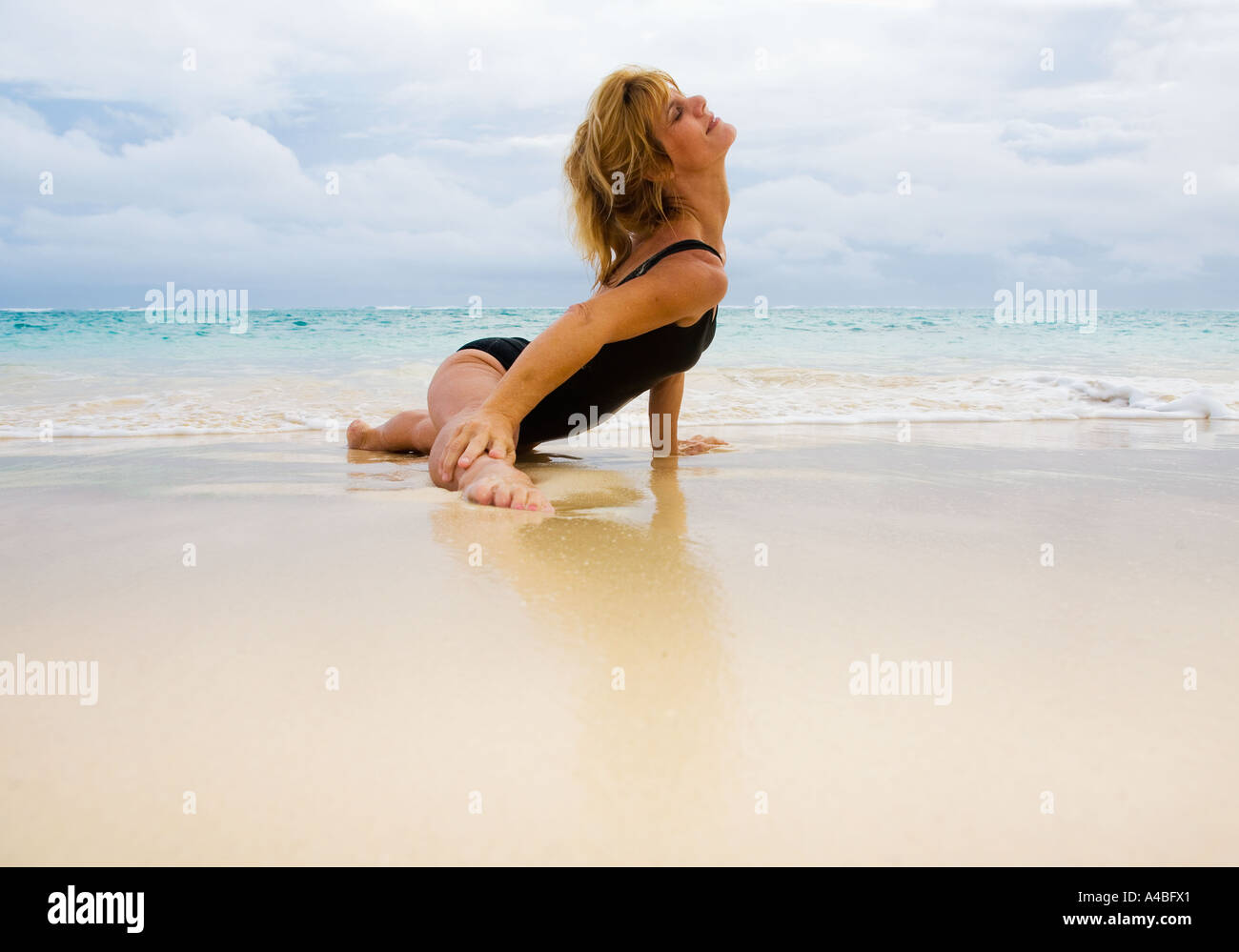 schöne 50 Jahre alte Frau beim Yoga am Strand Stockfoto