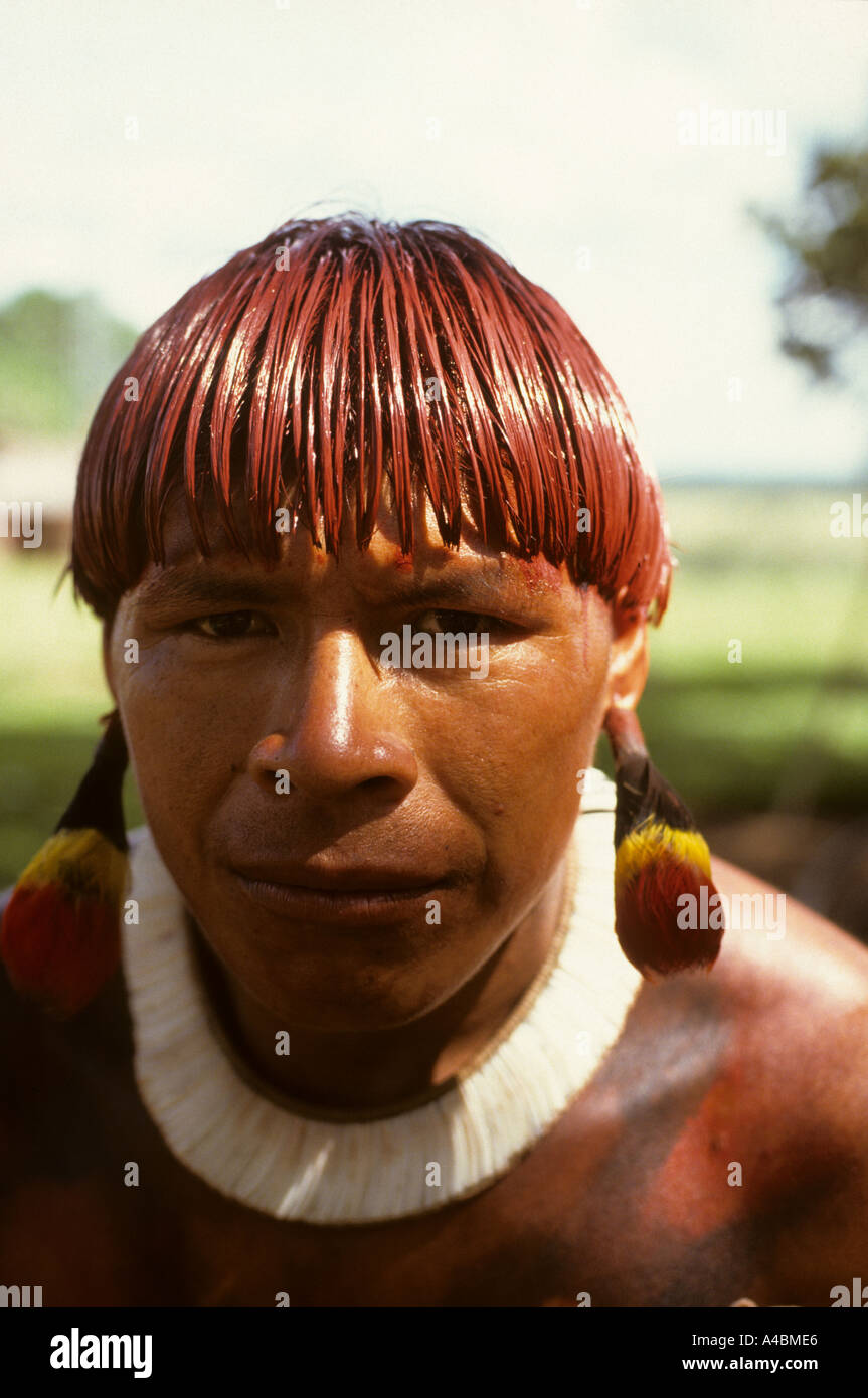 Posto Leonardo, Xingu, Brasilien. Mann mit Haar gefärbt mit roten Urucum Paste und bunte Feder Ohrringe; Xingu-Stamm. Stockfoto