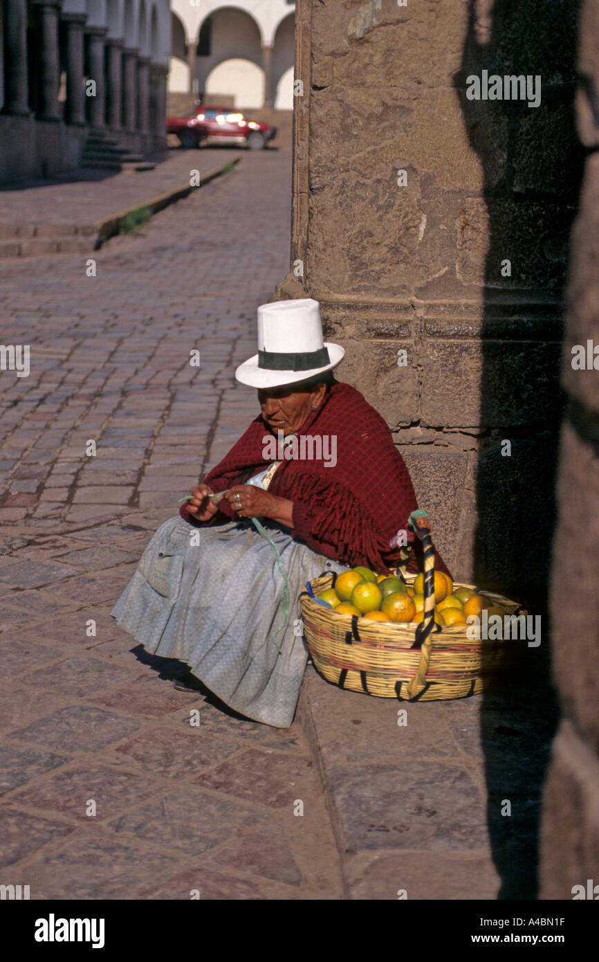 Cusco, Peru. Frau im traditionellen weißen Filzhut Orangen aus einem Korb auf der Ecke der Straße zu verkaufen. Stockfoto