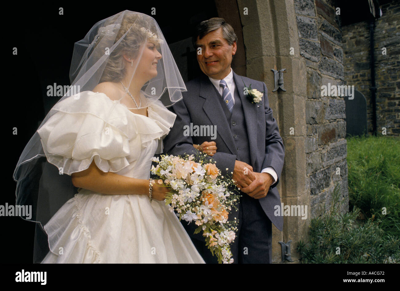 Braut in großen weißen Kleid mit rosa und weißen Blumenstrauß und Vater im  grauen Anzug mit weiße Corsage in kirchlichen Tür Vater schaut liebevoll  Braut Stockfotografie - Alamy