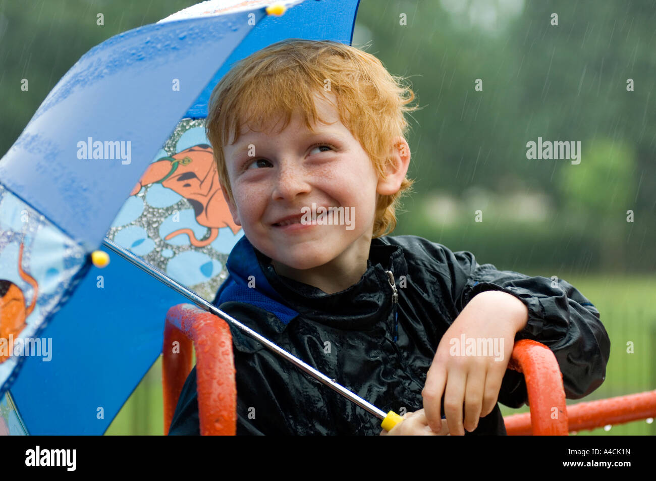 Junge blickte zu dem Regen immer nass versuchen, bleiben trocken unter einem Regenschirm Stockfoto