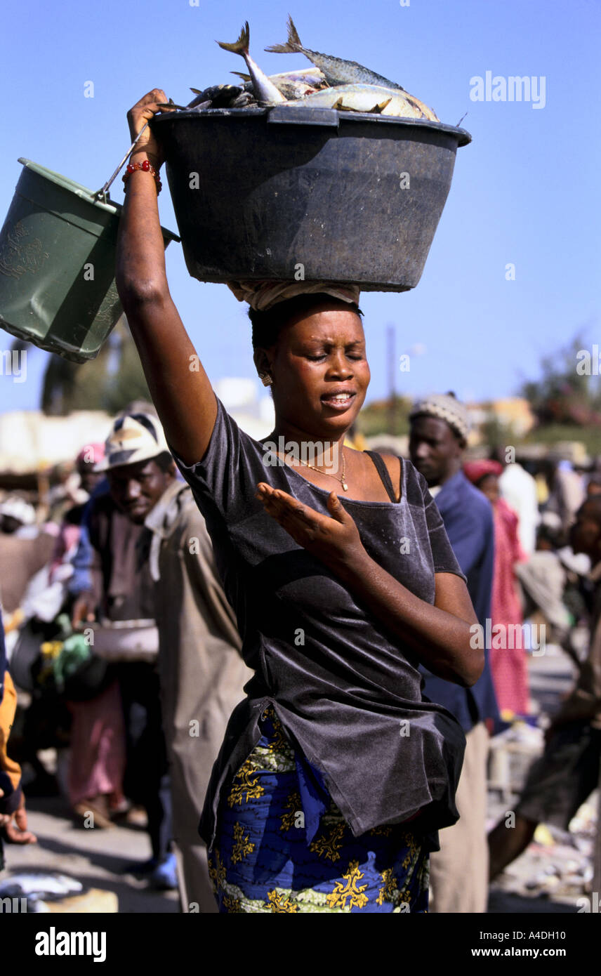 Eine Frau trägt einen großen Eimer mit Fisch auf dem Kopf auf dem Großmarkt.   Senegal, Westafrika Stockfoto