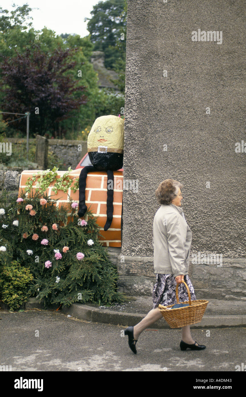 Eine Frau geht einkaufen, während Humpty Dumpty auf einer Mauer, weckt Königin Festival, Bradwell Dorf, Derbyshire sitzt Stockfoto