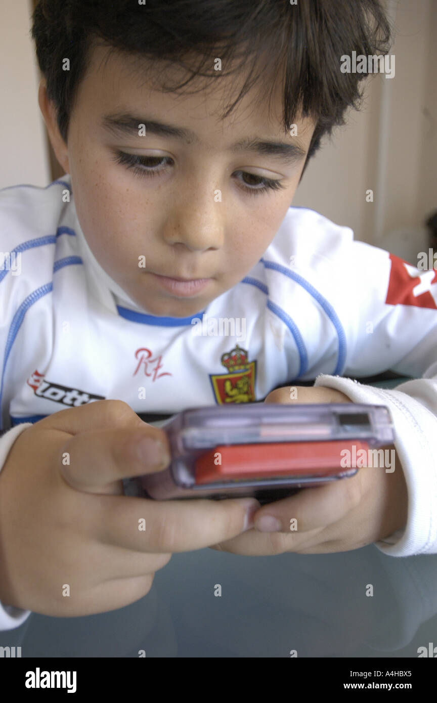 Acht Jahre alten spanischen junge Spiel Pokemon s mit einem Gameboy Color Computer mit Real Saragossa s Fußball gekleidet team un Stockfoto