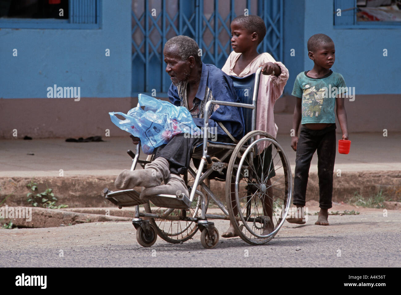 Kinder schieben eines Rollstuhls mit einem behinderten Verwandten zum Betteln auf den Straßen von Moshi, Tansania Stockfoto
