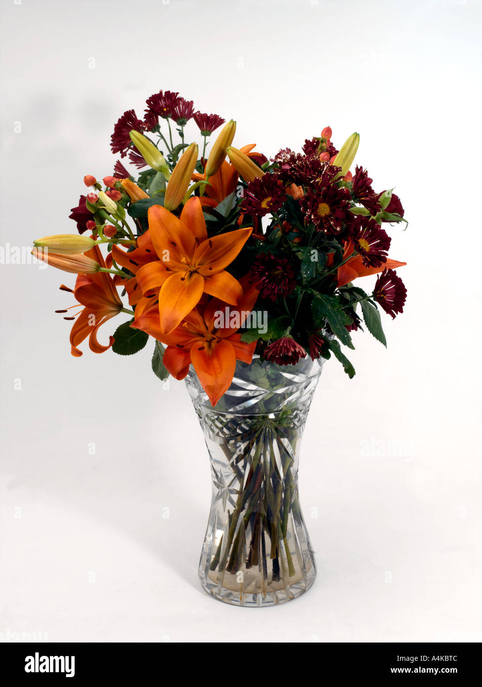 Vase mit Blumen Orange Lilien und lila Margeriten mit Glitzer in führen Kristallvase Stockfoto