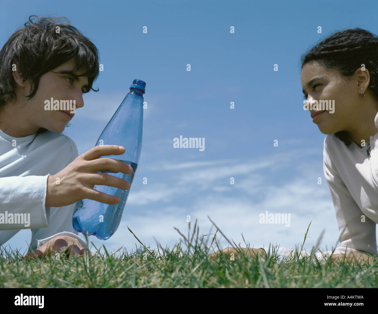 Junger Mann und junge Frau stützte sich auf Ellenbogen in Rasen, jungen Mann hielt Flasche Stockfoto