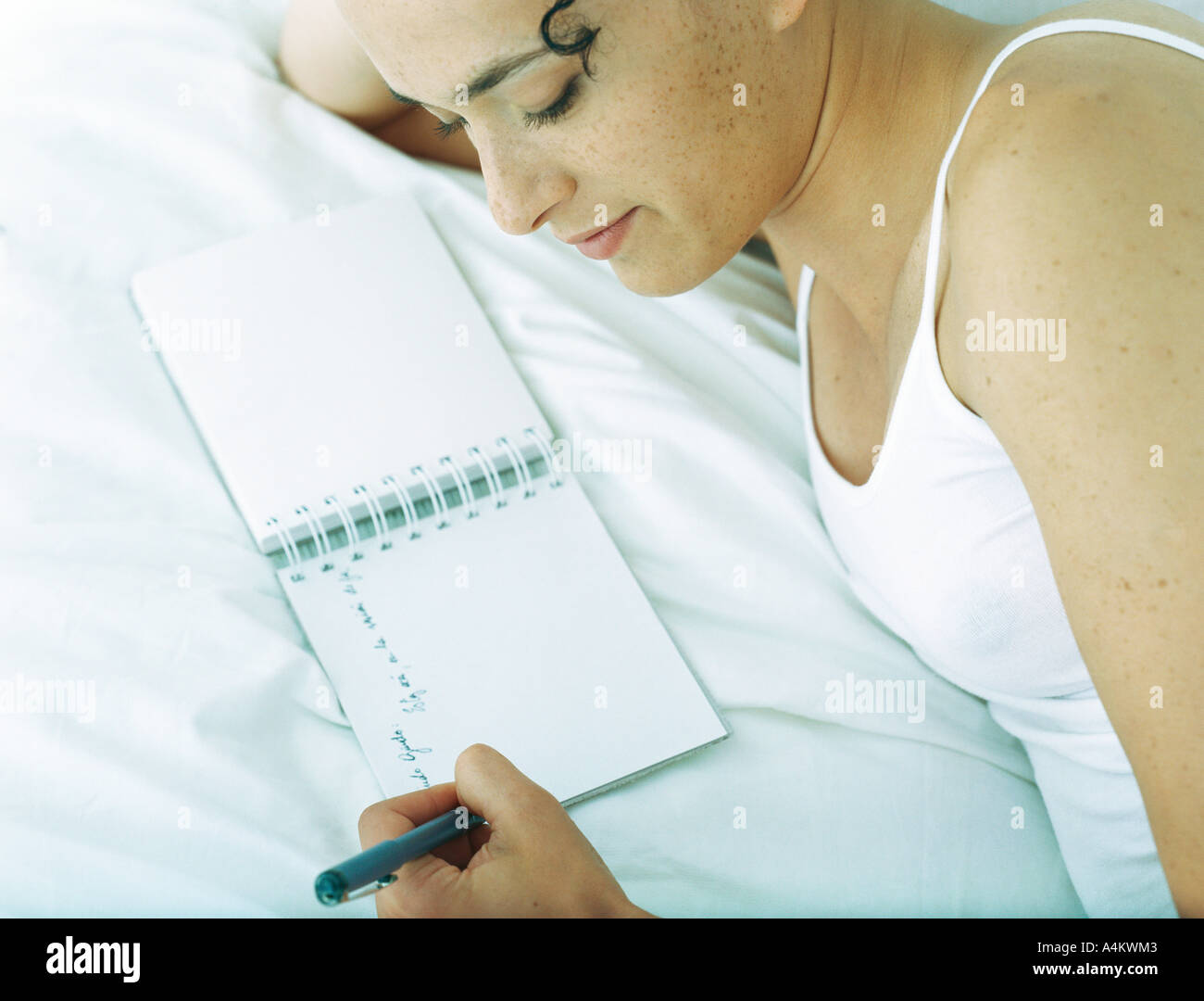Frau liegt seitlich am Bett im Notizbuch mit Stift schreiben Stockfoto