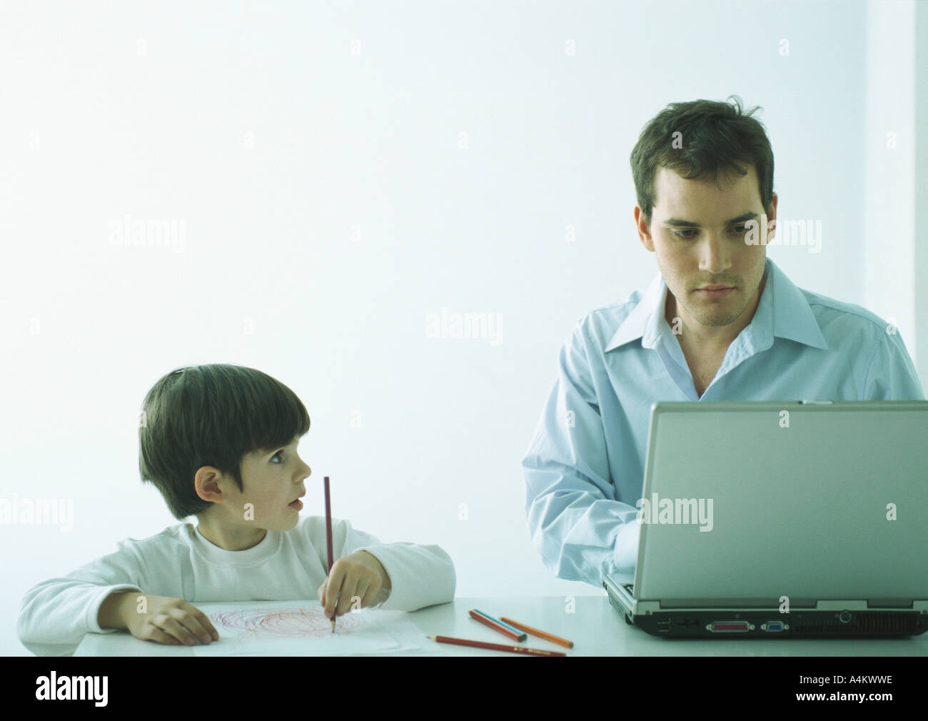 Mann, sitzend am Tisch arbeiten am Laptop, junge sitzt neben ihm Färbung mit Bleistiften Stockfoto