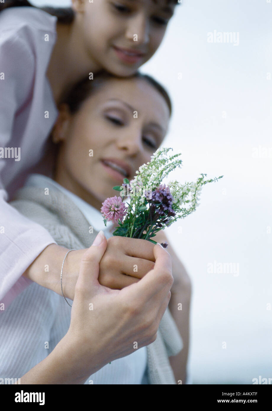 Mädchen, die Mutter von hinten, die Hand der Mutter über des Mädchens zu umarmen, halten Bouquet von Wiesenblumen Stockfoto