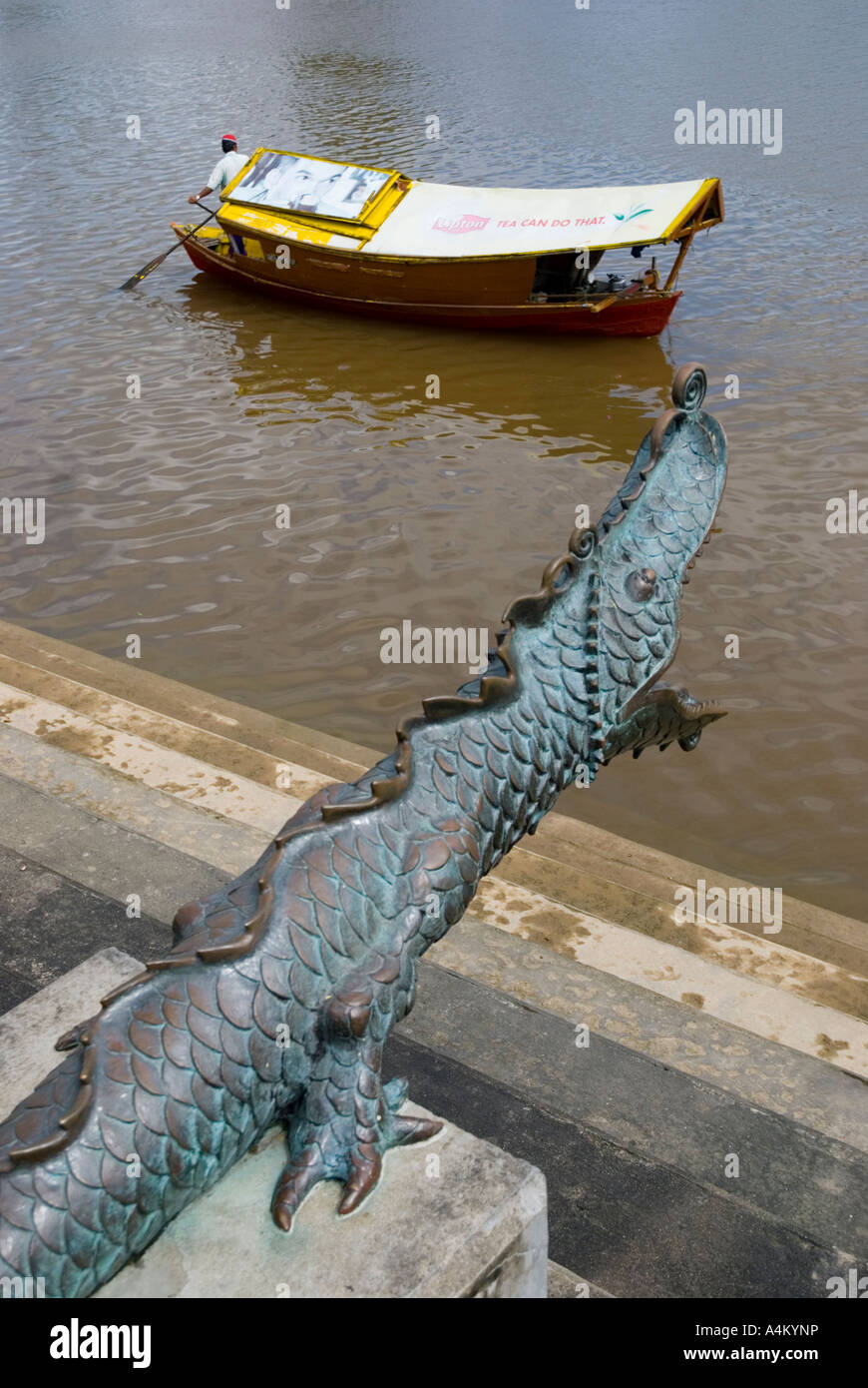Ein Fährmann auf dem Fluss bei Kuching reiht an einer Replik chinesischer Bronzekanone in Form eines feuerspeienden Drachen vorbei Stockfoto