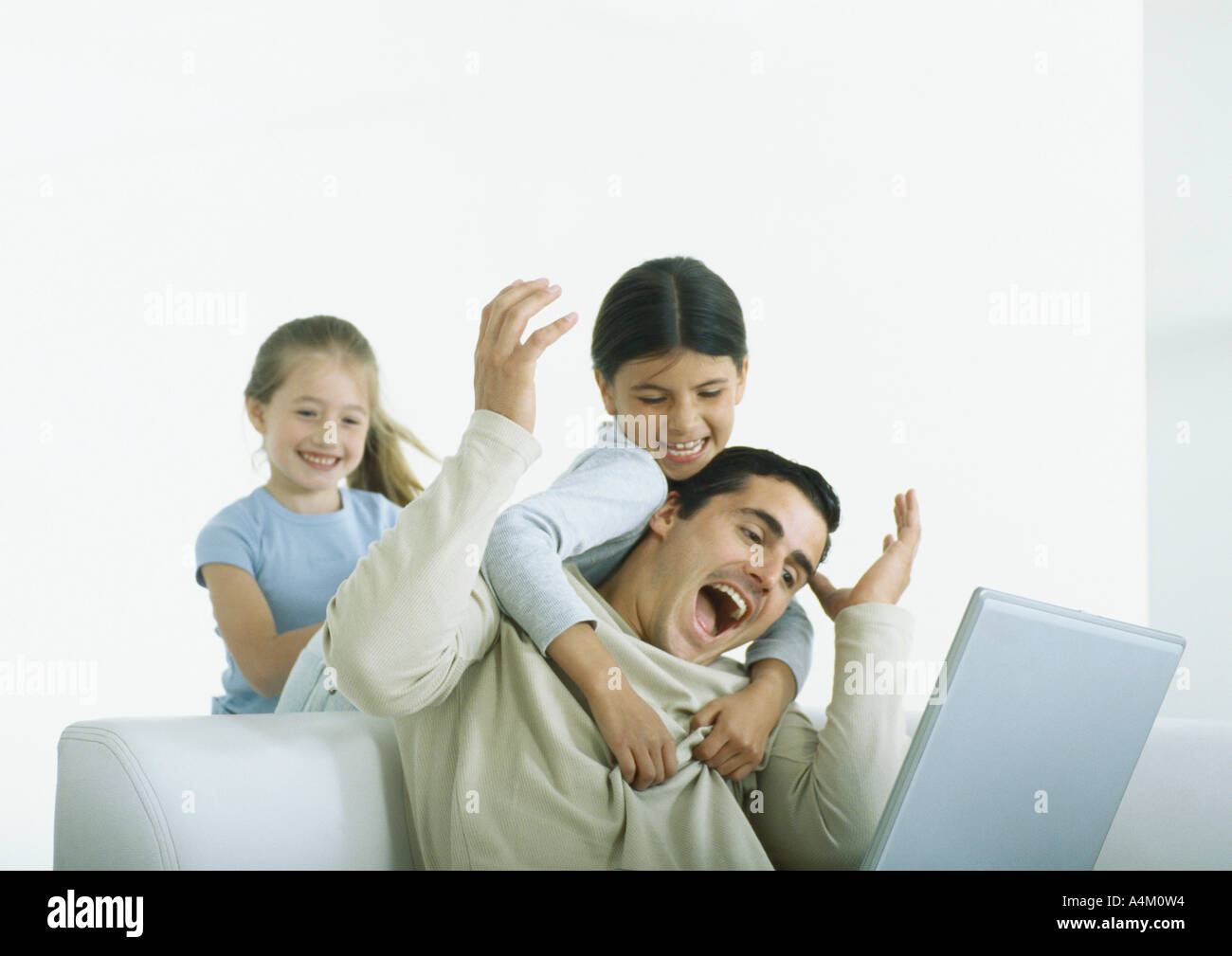 Zwei Mädchen hinter Mann, sitzend mit Laptop, mit Arme um ihn Stockfoto