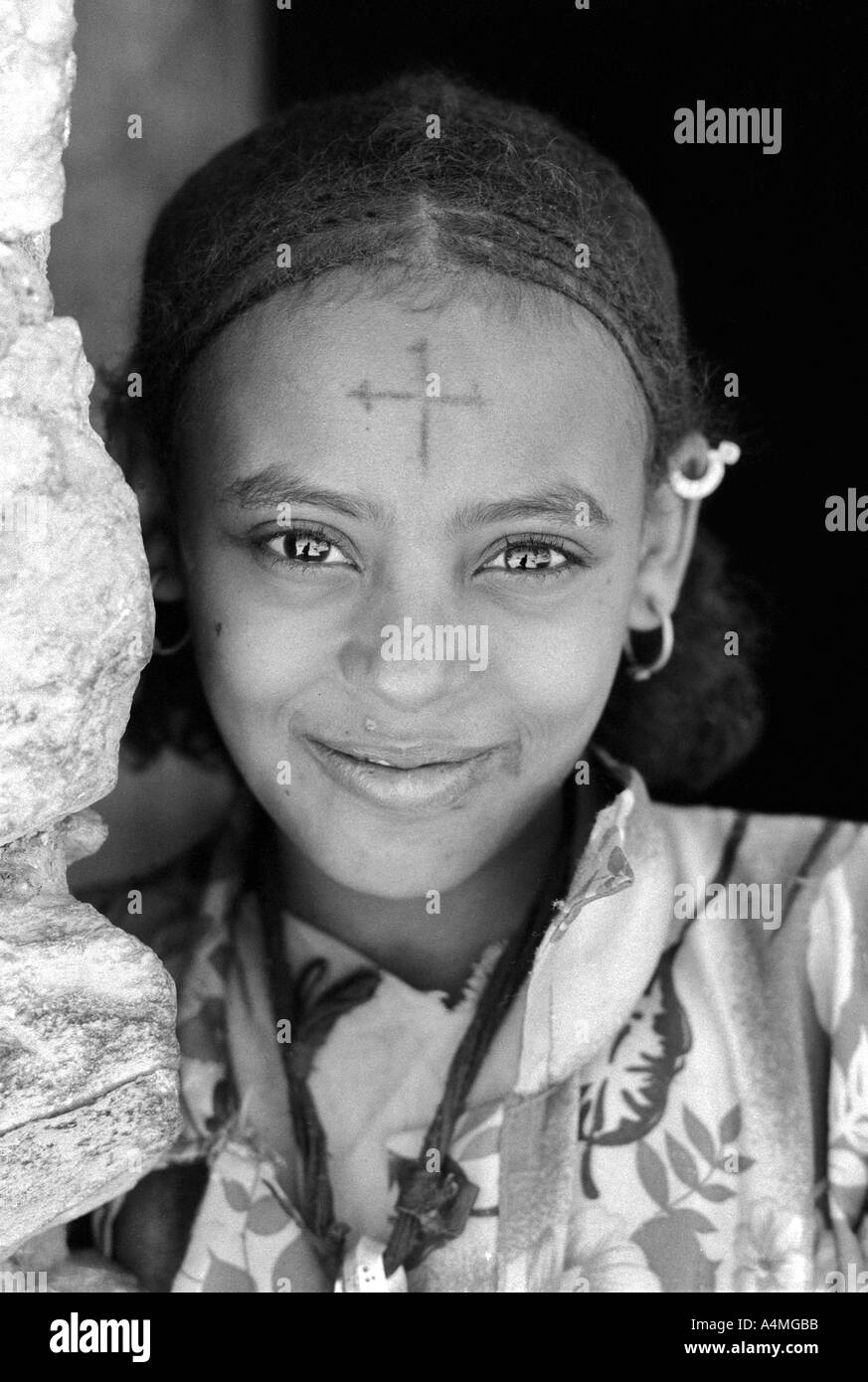 S/W-Porträt eines lächelnden Mädchens mit flüssigen Augen, traditioneller Frisur und einem koptischen christlichen Kreuz auf der Stirn. Adua, Äthiopien, Afrika Stockfoto