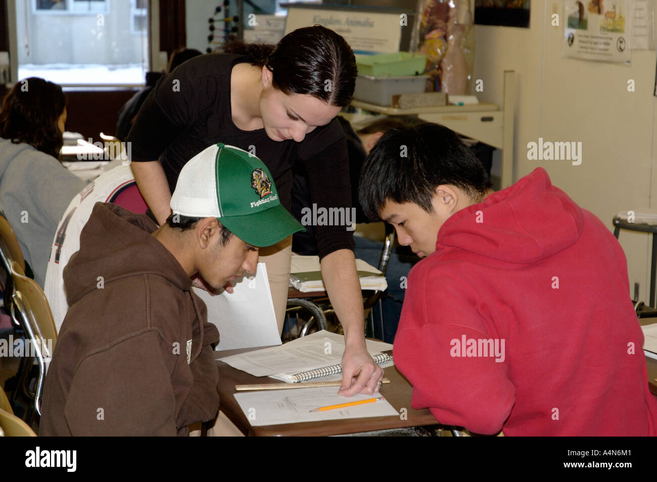 Junge Lehrerin helfen zwei asiatische Studenten mit Schularbeiten im Klassenraum Stockfoto