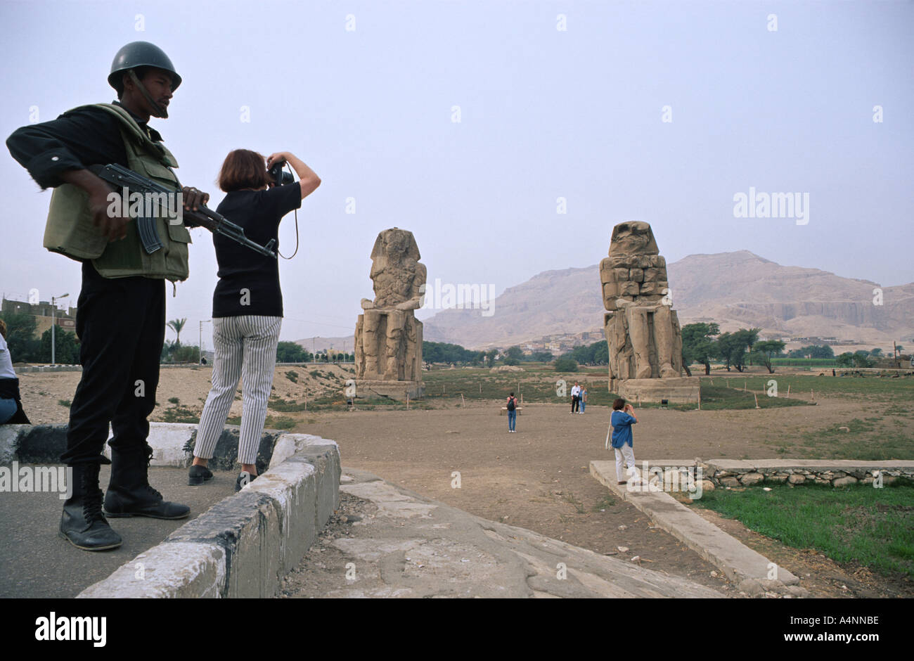 Touristen machen Sie Schnappschüsse unter enger Bewachung eines ägyptischen Soldaten an den Memnon Kolossen Stockfoto