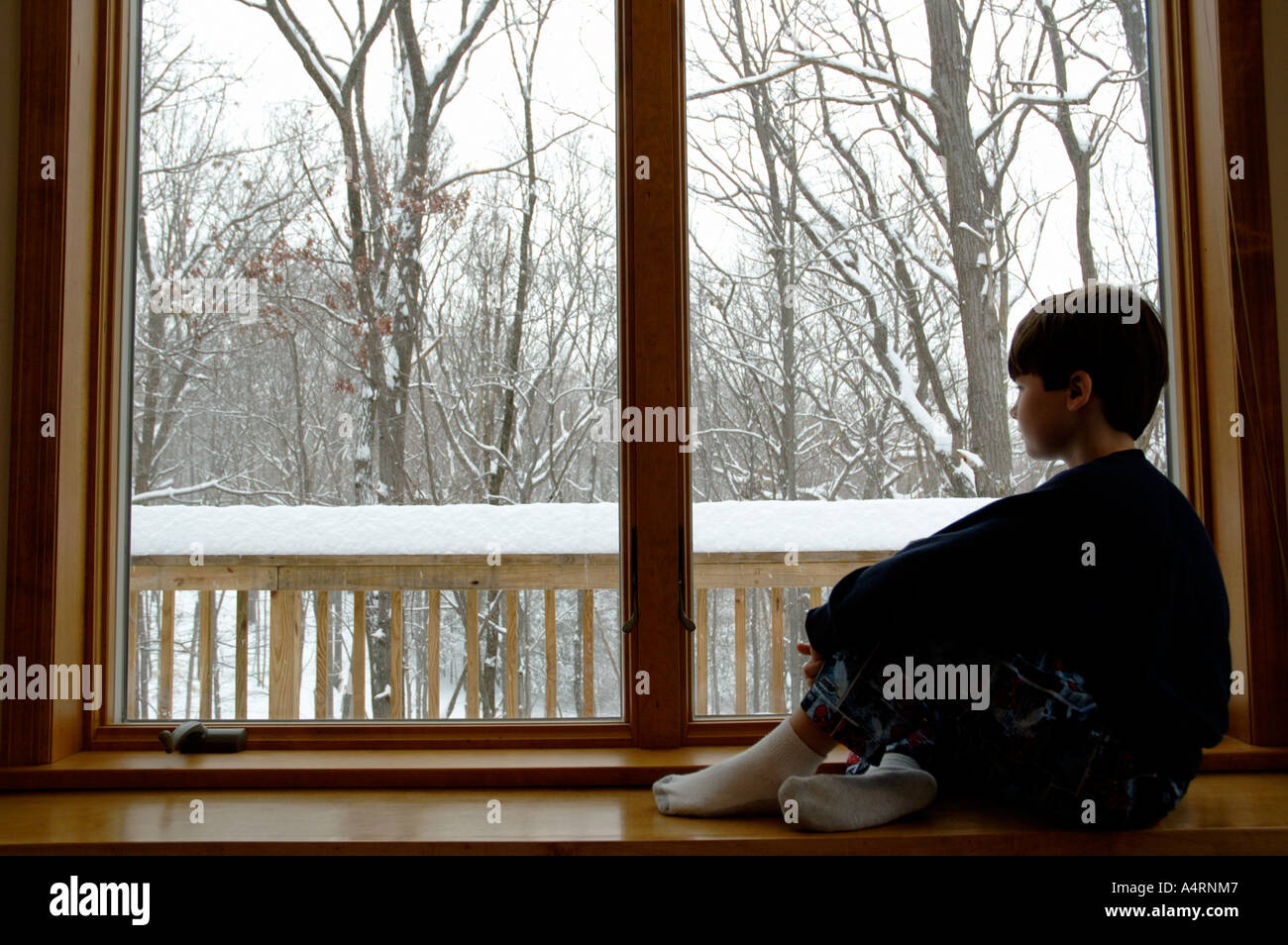 Kleiner Junge schaut aus Fenster an einem grauen Schneetag Stockfoto