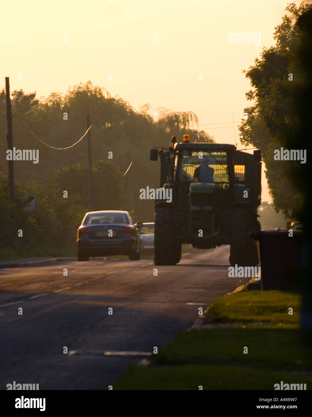 Auto und Traktor auf einer Straße bei Sonnenuntergang Stockfoto