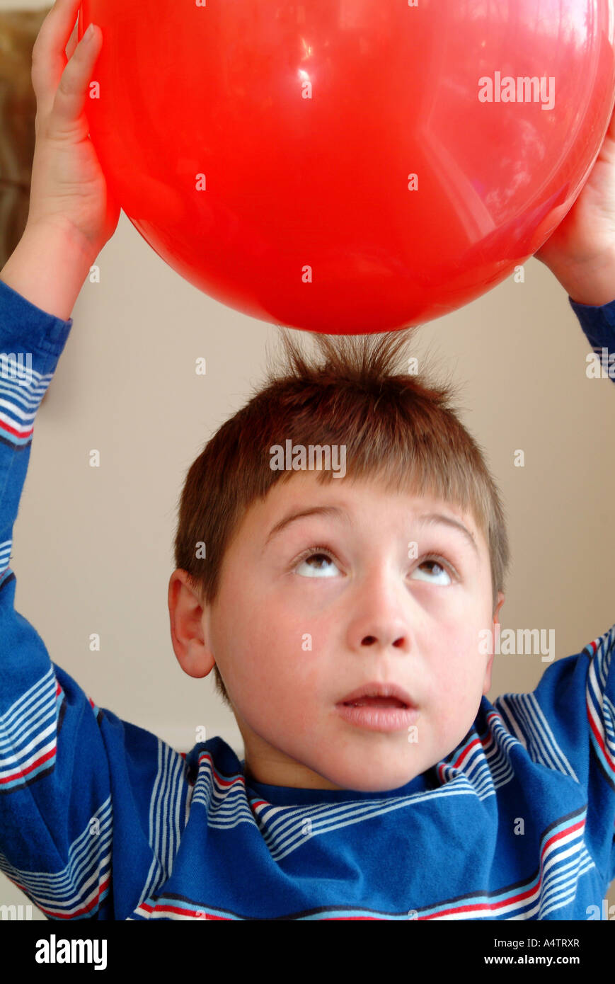 Ein 7 Jahre alter Junge hält einen roten Ballon über seinen Kopf und statische Elektrizität zieht seine Haare in Richtung der Ballon Stockfoto