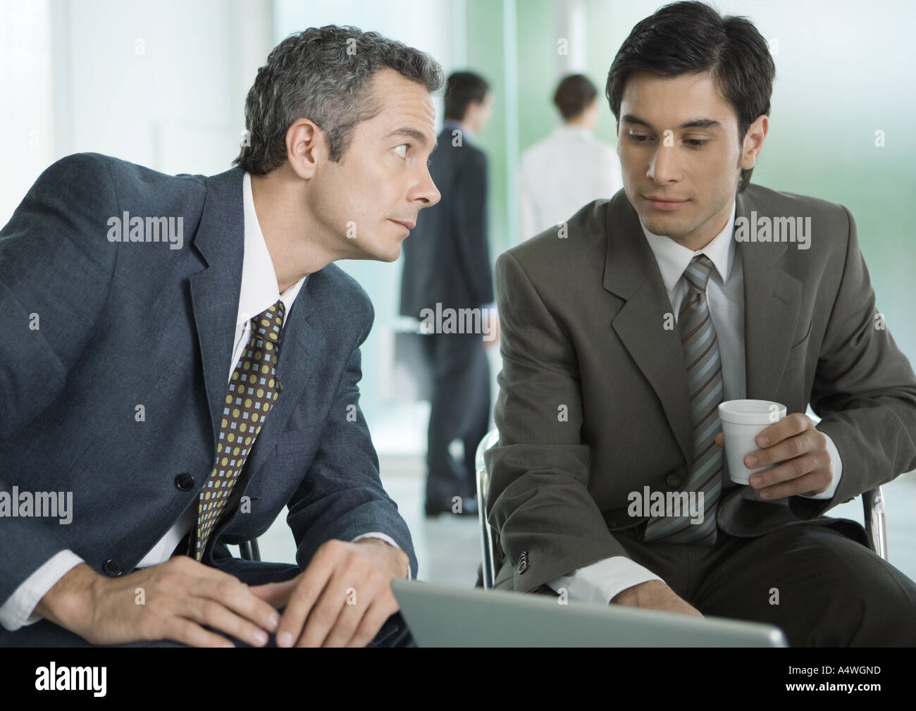 Zwei Geschäftsleute sitzen um einen Laptop, eine Kaffeetasse Stockfoto