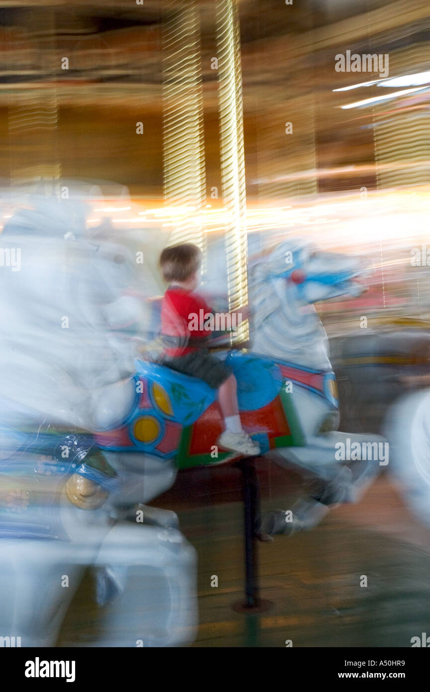 Ein Junge, der auf einem beweglichen Frohe Runde/Karussell/Pferd allein mit Motion Blur gehen in einem Vergnügungspark oder State Fair Stockfoto