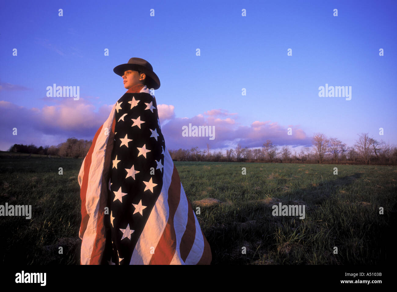 Junge in Coyboy Hut und eingewickelt in amerikanische Flagge im Feld bei Abenddämmerung Blick in Richtung Horizont Upstate New York USA Stockfoto