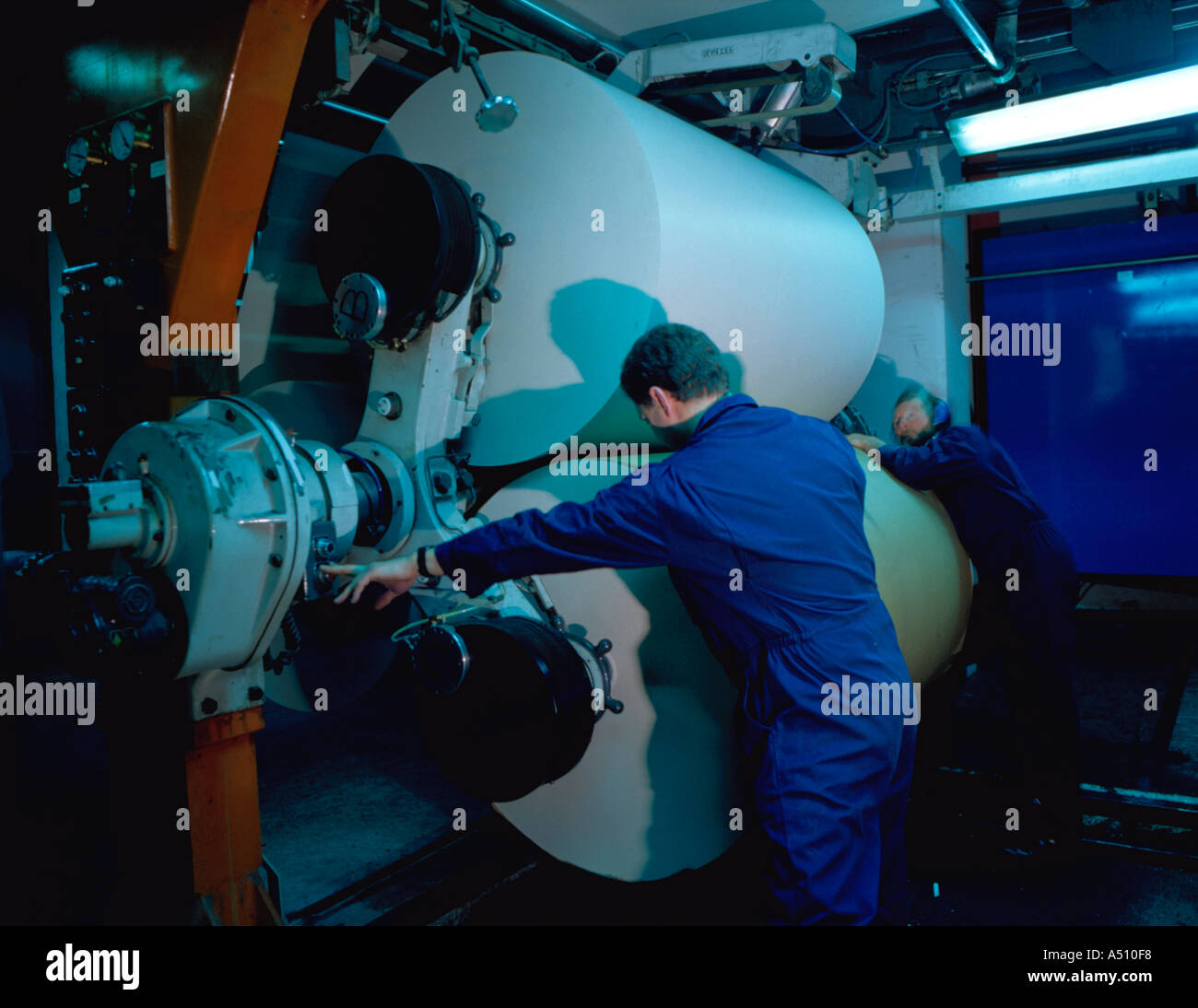 Männer laden Papierrollen auf einer Zeitungsdruckmaschine. Stockfoto