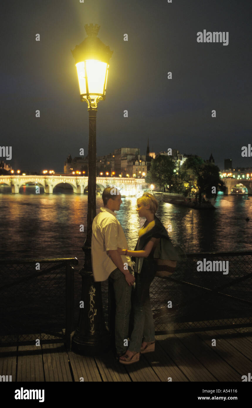 Junges Paar auf der Pont des Arts mit Fluss und Pont Neuf hinter in der Nacht Stockfoto